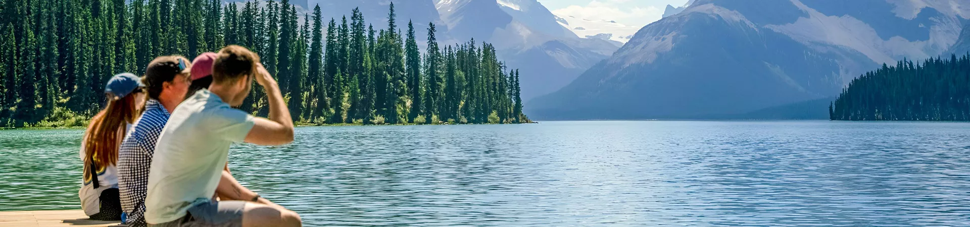 People Sitting Close To A Lake Enjoying The Snowy Mountains View