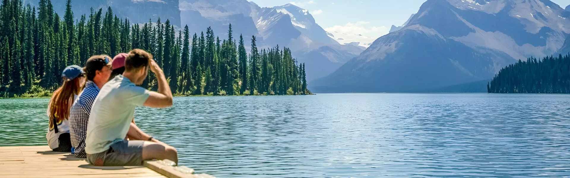 People Sitting Close To A Lake Enjoying The Snowy Mountains View