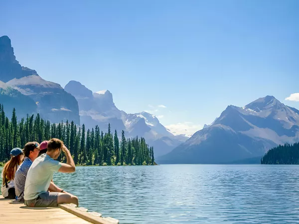 People Sitting Close To A Lake Enjoying The Snowy Mountains View