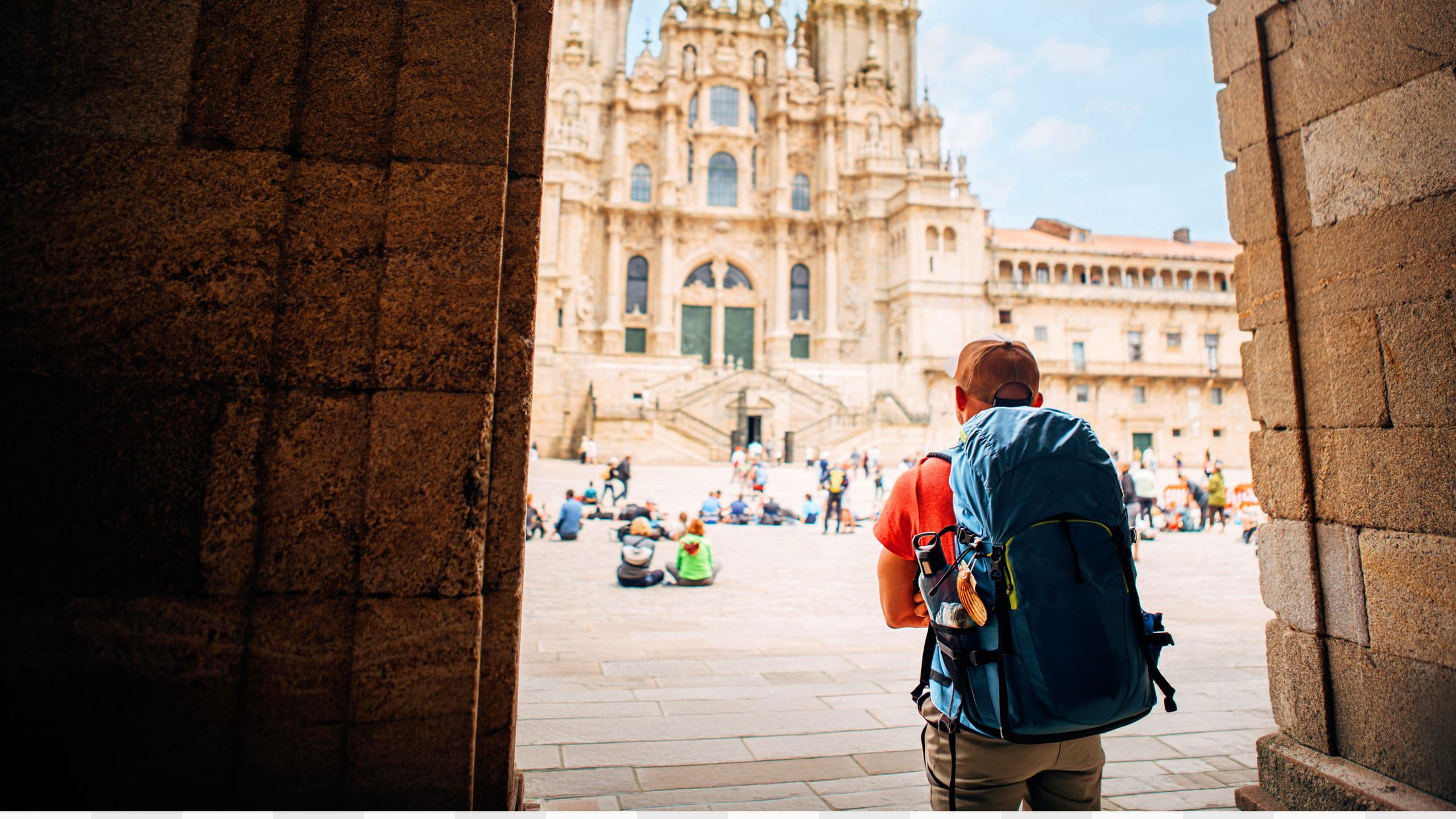Hiker with backpack arriving at the Cathedral of Santiago de Compostela and Plaza del Obradoiro at the end of the Camino de Santiago Spain - Contiki Hiking Camino Tour