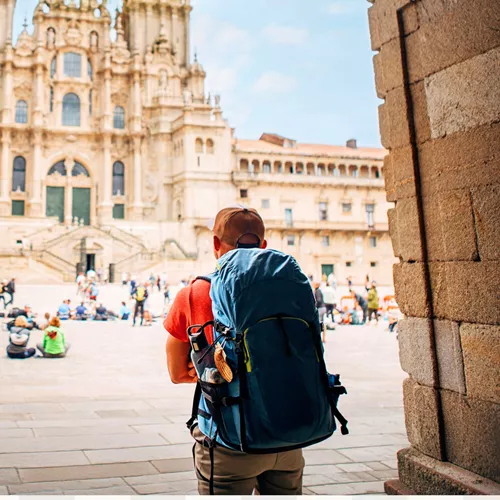 Hiker with backpack arriving at the Cathedral of Santiago de Compostela and Plaza del Obradoiro at the end of the Camino de Santiago Spain - Contiki Hiking Camino Tour