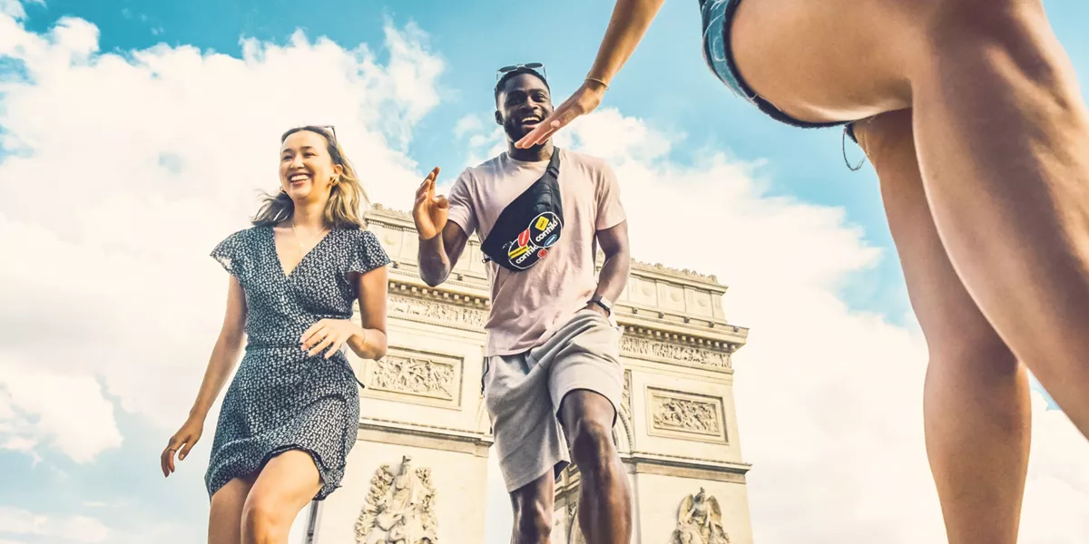 Contiki travellers laugh and high-five in front of the Arc de Triomphe in Paris during the London to Athens Tour