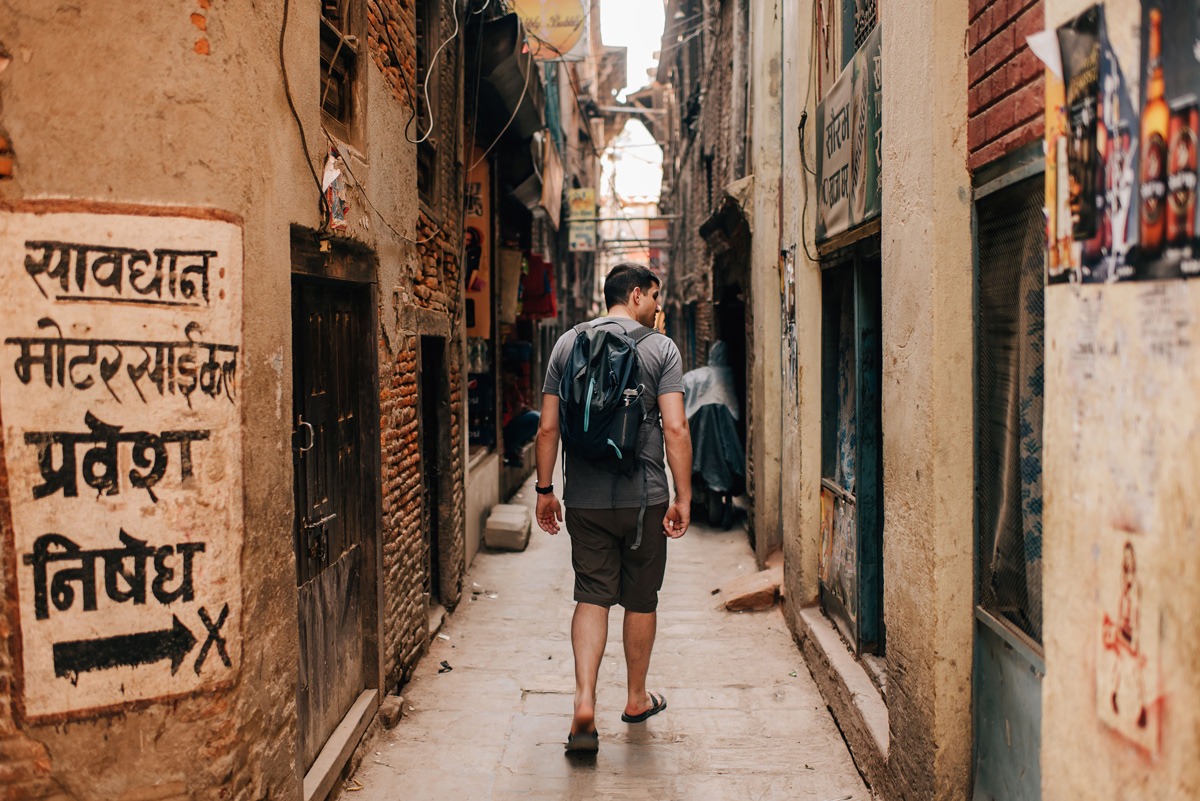 Man walking in a narrow road red brick buildings in Nepal.