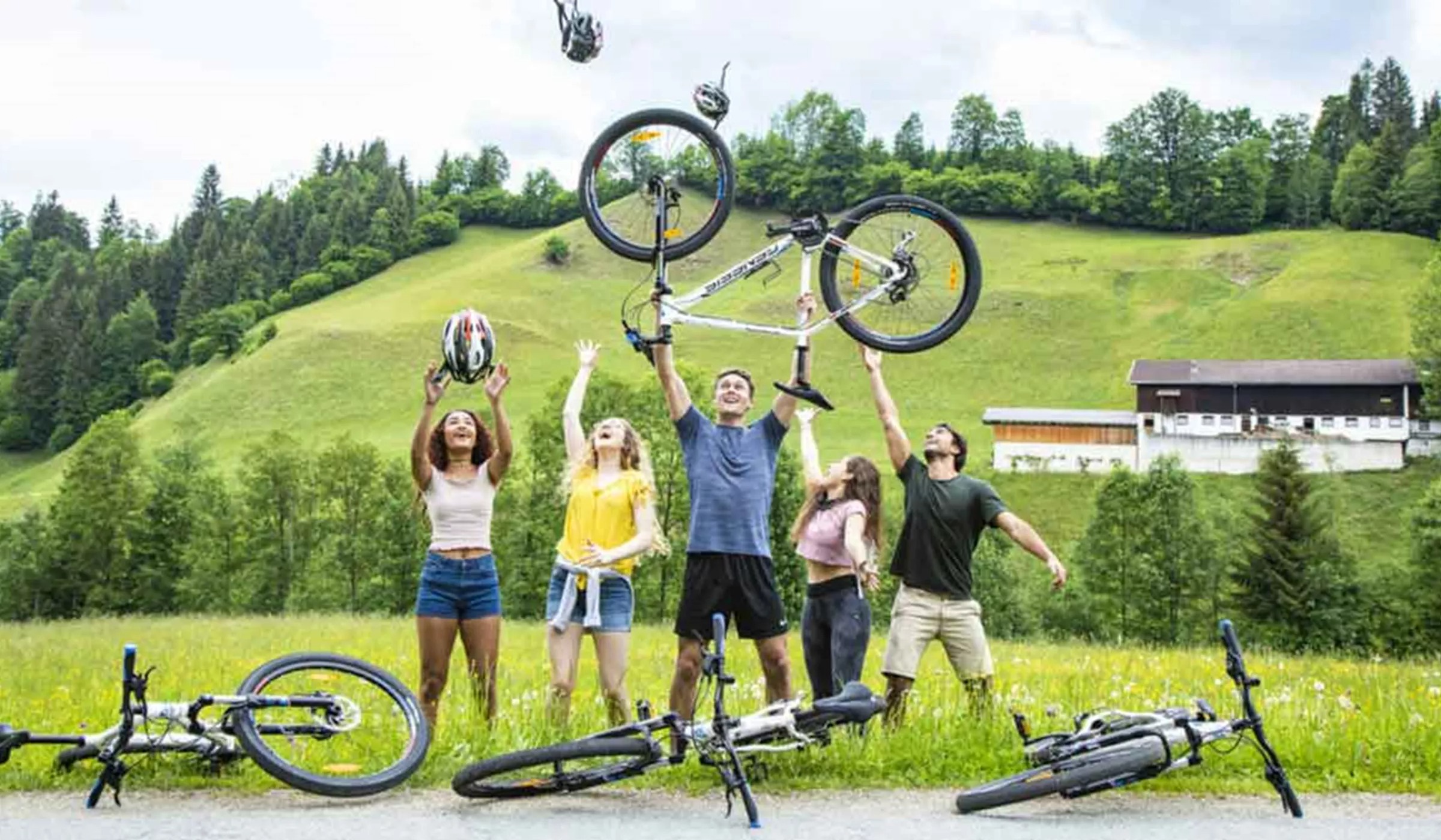 Group Of Young Travelers Throwing Bike In Air Austria