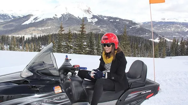 Smiling woman in a red helmet sitting on a snowmobile