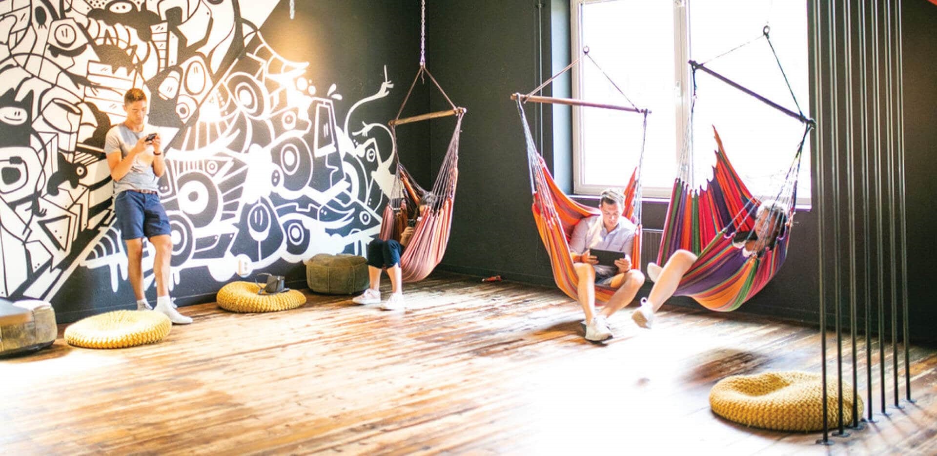 A group of people resting in a room with pillows and hanging hammocks