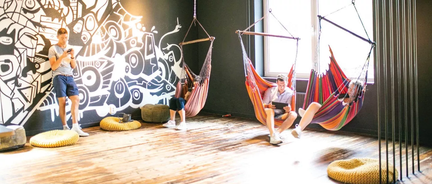 A group of people resting in a room with pillows and hanging hammocks