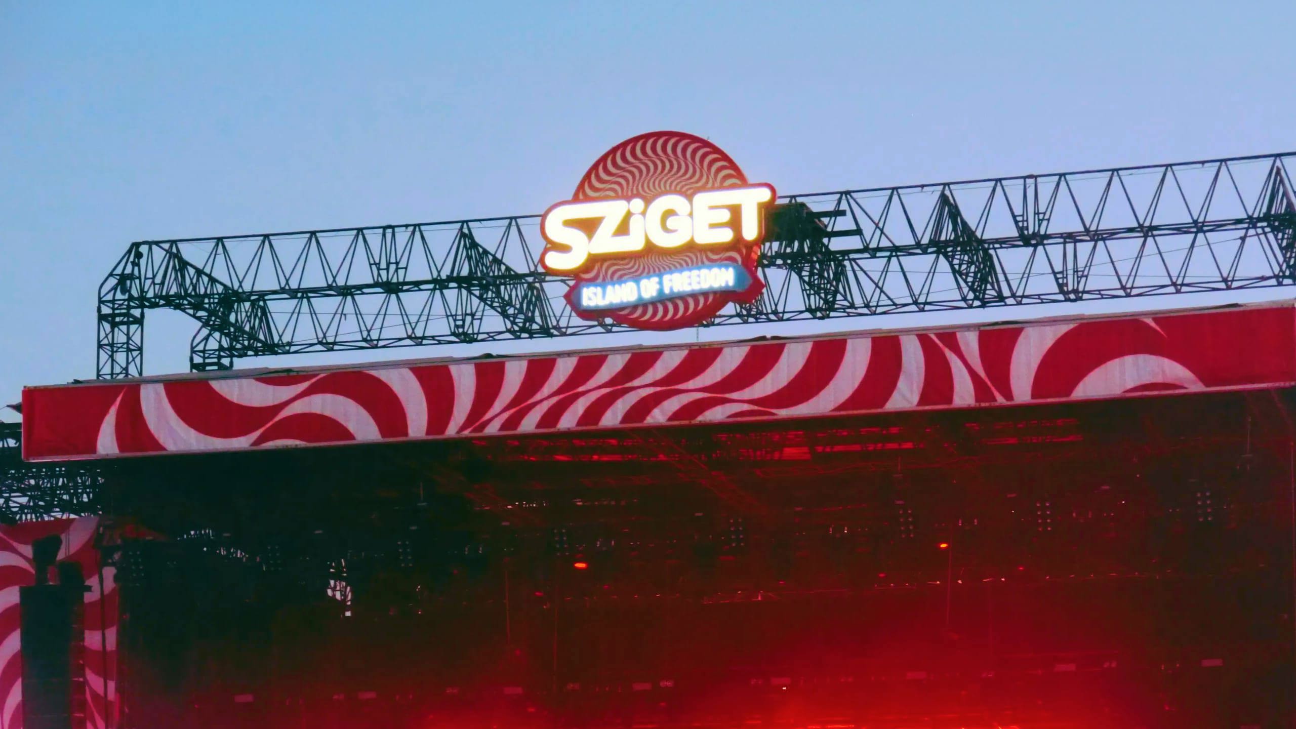 Sziget Festival main stage at dusk in Budapest Hungary with illuminated logo and red swirl stage design - Contiki Europe Festival Tour