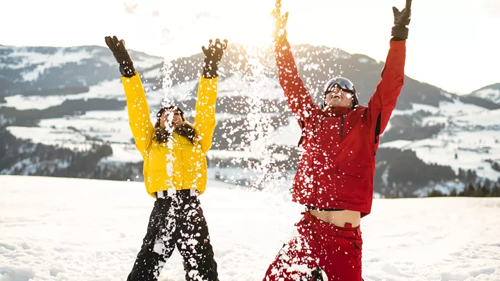 Travellers playing in the snow in front of the Alps in Hopfgarten, Austria