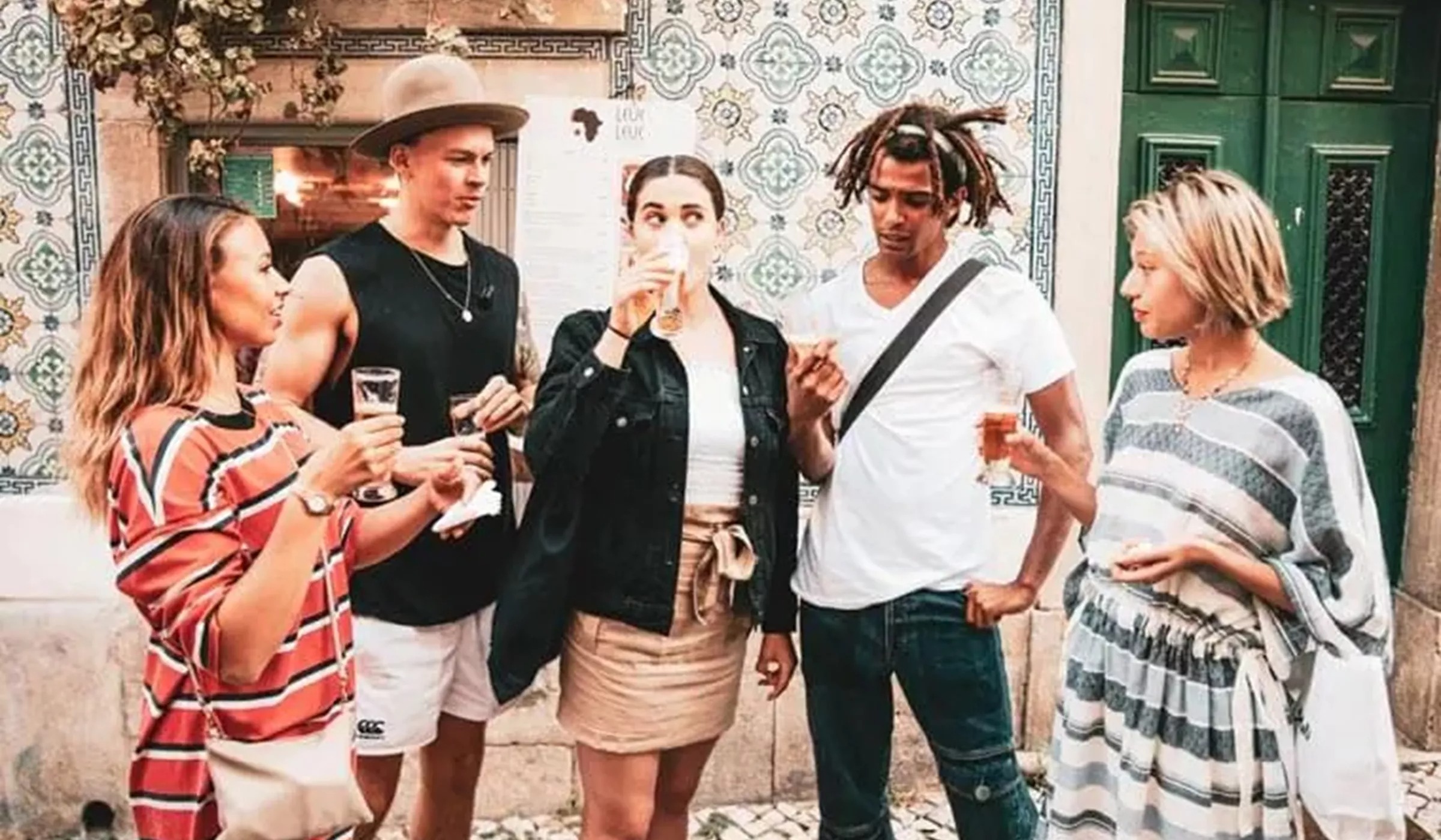 Group of young people drinking while standing outside in front of building with mosaic on wall