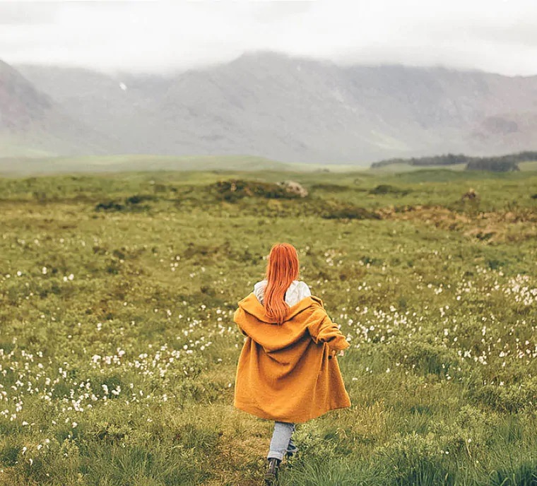 Red-haired girl walking on the meadow