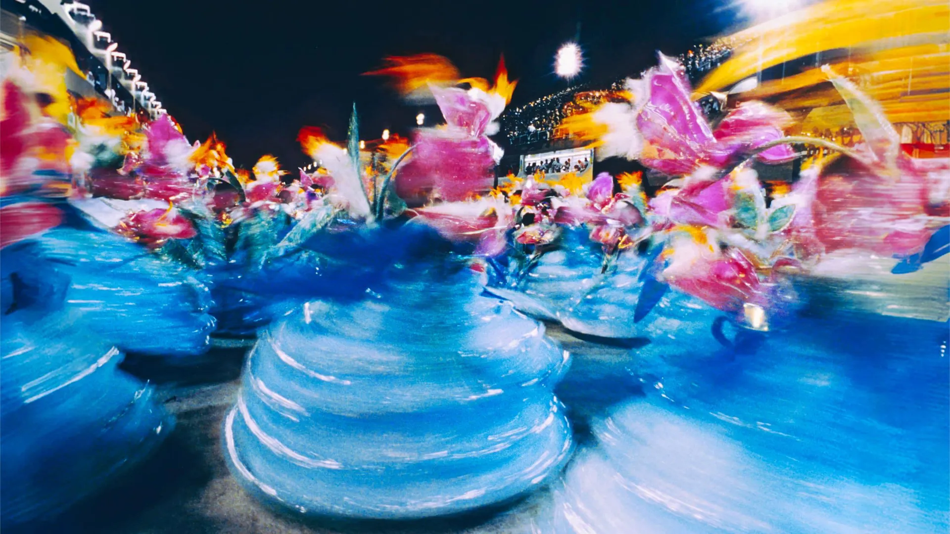 Colourful Carnival performers in elaborate costumes spin through a parade during Carnival celebrations in Brazil at night