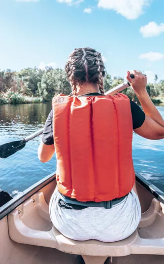 A Contiki travellers paddles a canoe across calm waters, surrounded by native bushland and mirrored reflections in the peaceful wetlands - Sydney to Noosa Tour