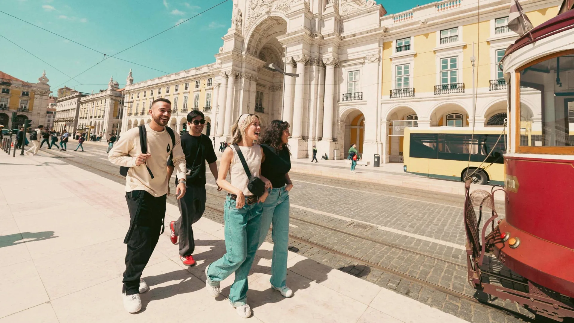 Contiki travellers exploring Lisbon’s Praça do Comércio beside the iconic yellow tram, discovering historic landmarks on the Spain & Portugal Panorama Tour