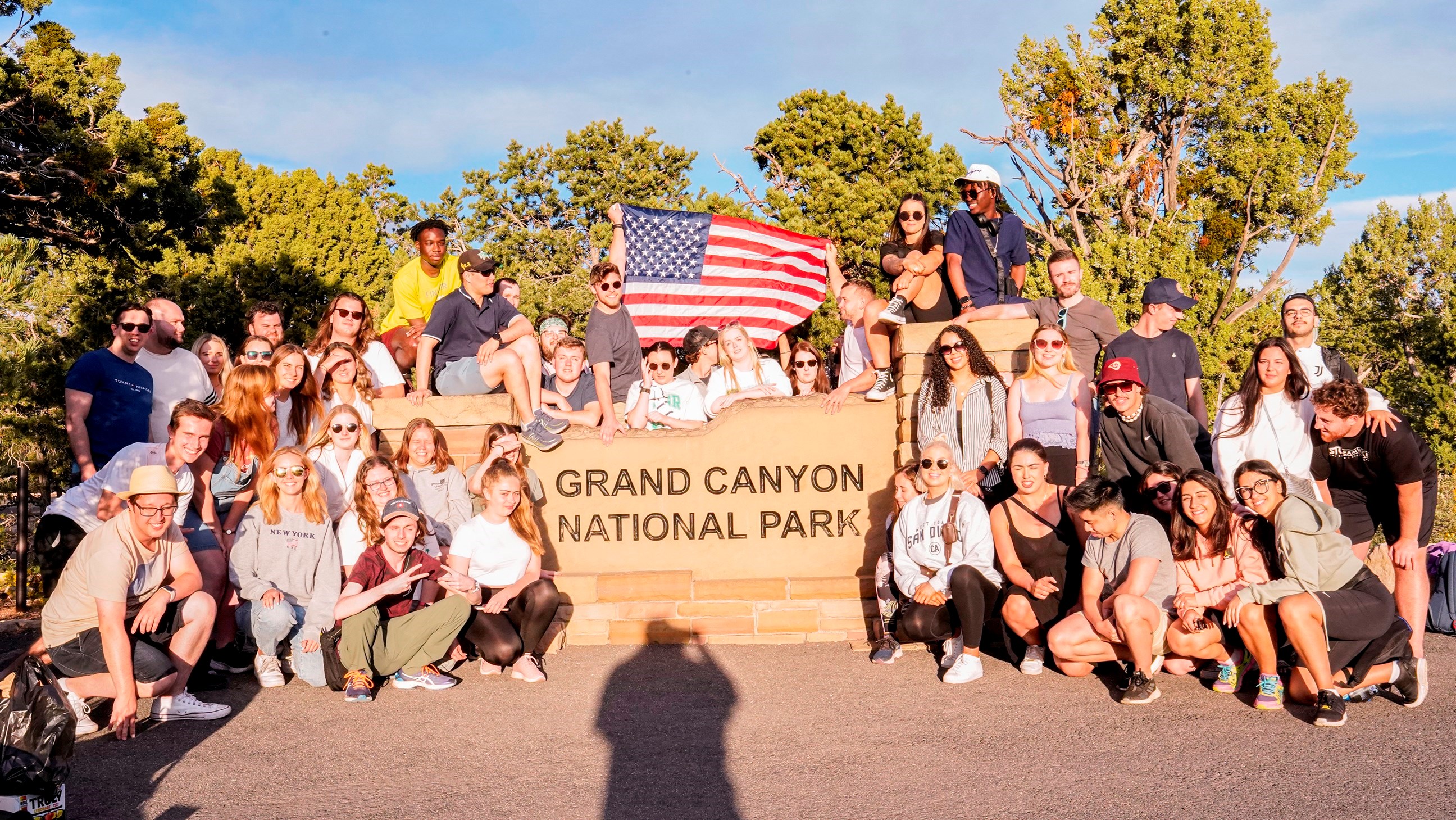 Group of Travellers Sat and Stood around the Grand Canyon National Park Sign, Arizona