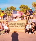 Group of Travellers Sat and Stood around the Grand Canyon National Park Sign, Arizona