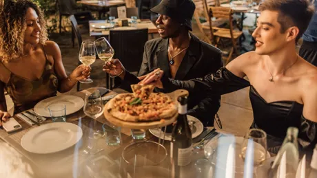 A group of people sitting around a table eating pizza and drinking wine
