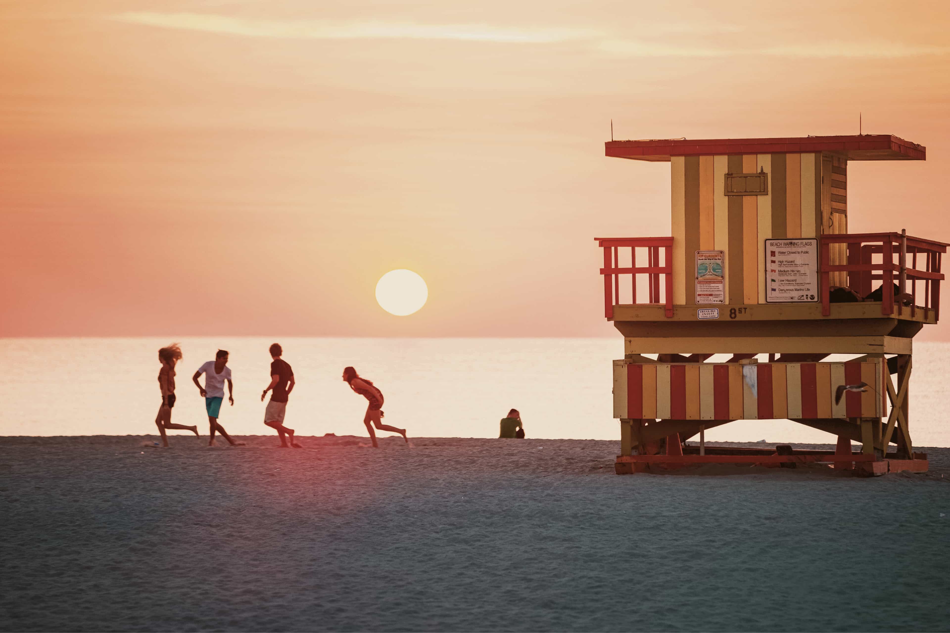 Travellers running along the sand beside a colourful lifeguard tower at sunset, Miami Beach, USA.