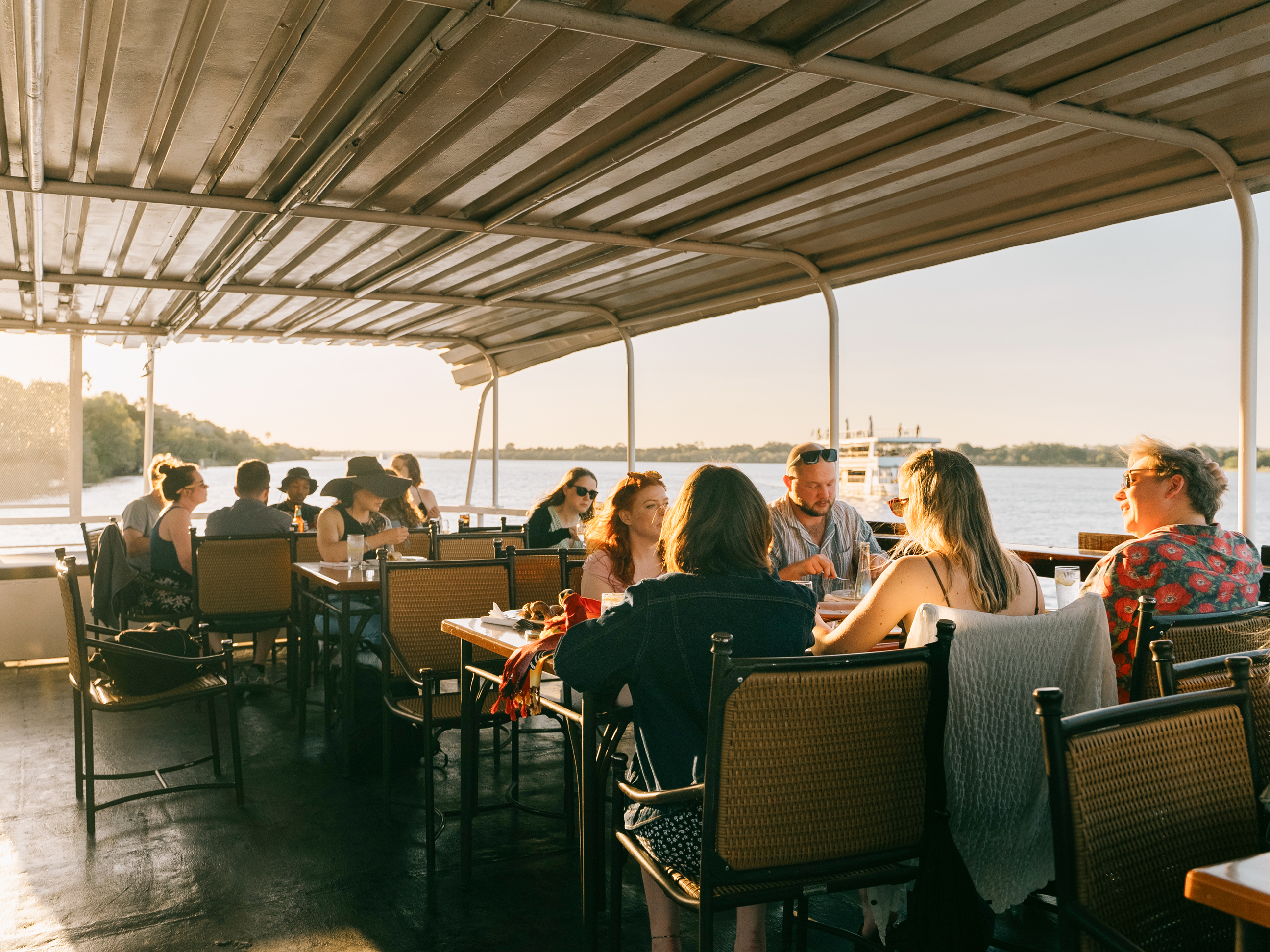 Travellers enjoying drinks at table on a sunset cruise on the Zambezi river, Zambia