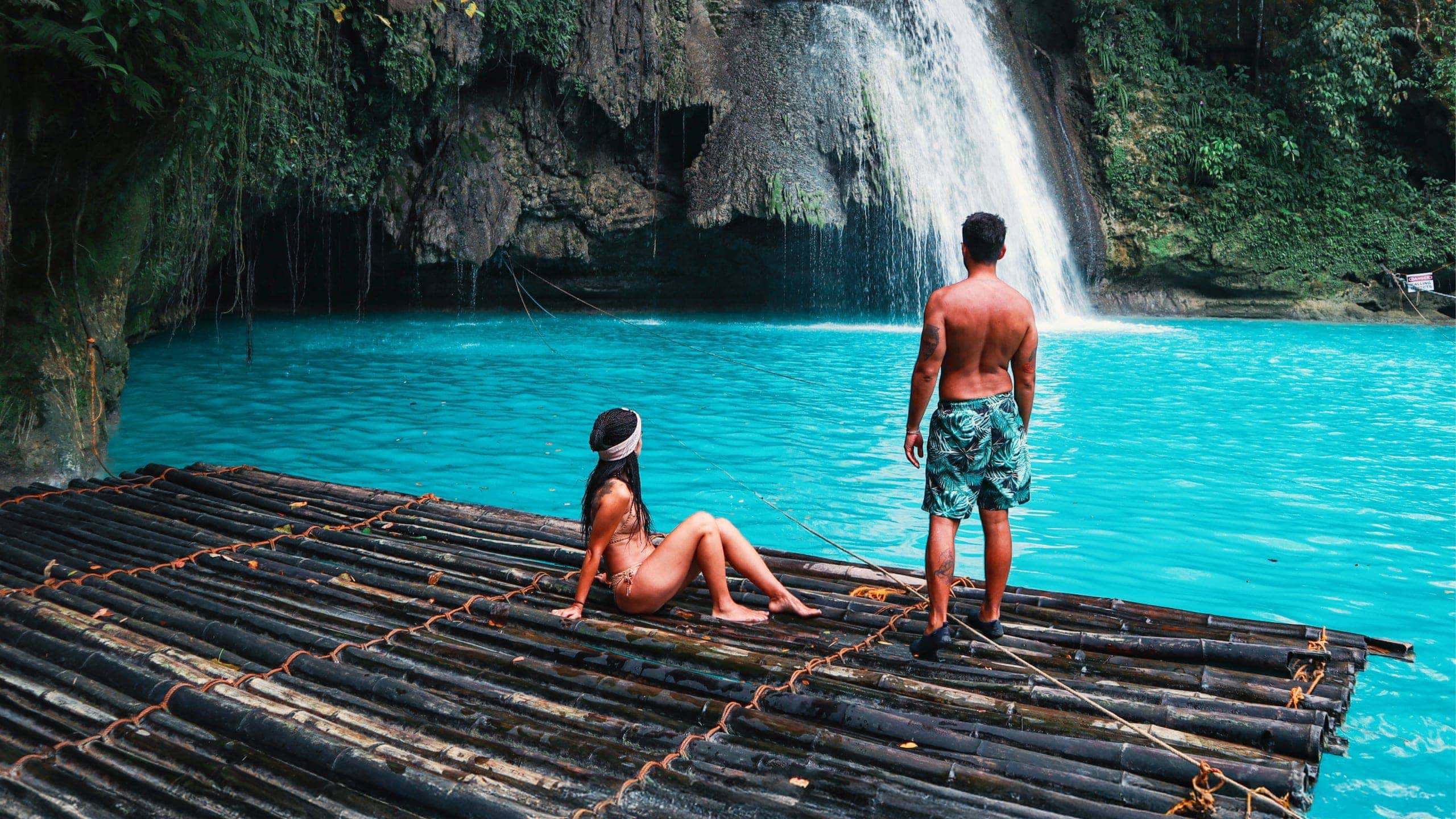 Two travellers on a bamboo raft at the base of Kawasan Falls with vivid turquoise water in Cebu Philippines - Contiki Cebu Bohol and Boracay Island Hopper Tour