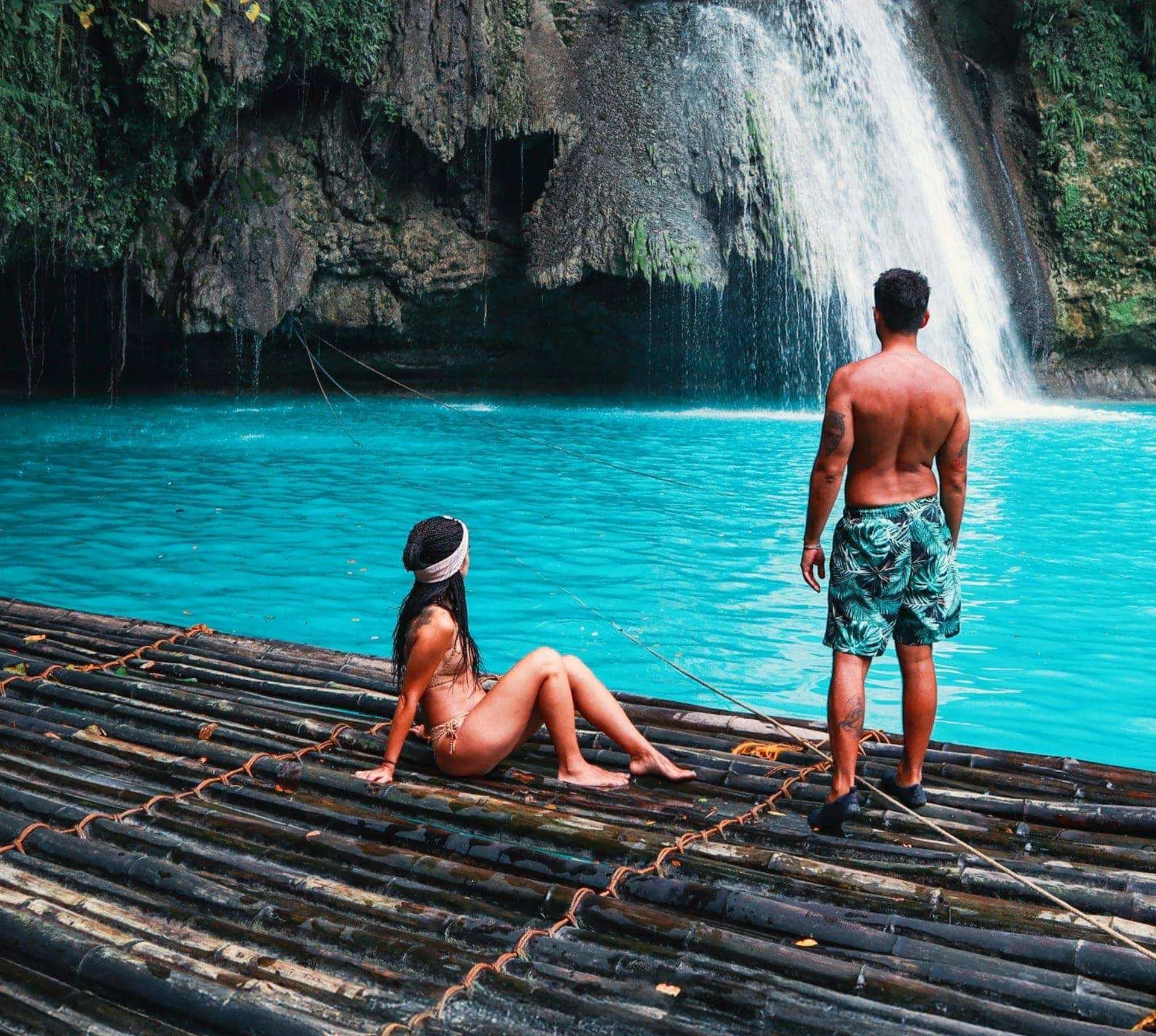 Two travellers on a bamboo raft at the base of Kawasan Falls with vivid turquoise water in Cebu Philippines - Contiki Cebu Bohol and Boracay Island Hopper Tour