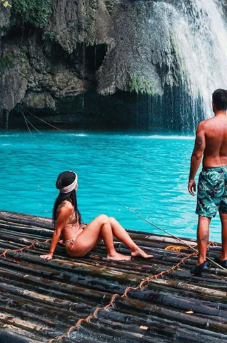 Two travellers on a bamboo raft at the base of Kawasan Falls with vivid turquoise water in Cebu Philippines - Contiki Cebu Bohol and Boracay Island Hopper Tour