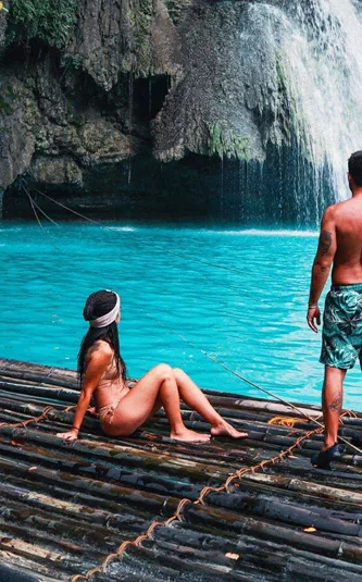Two travellers on a bamboo raft at the base of Kawasan Falls with vivid turquoise water in Cebu Philippines - Contiki Cebu Bohol and Boracay Island Hopper Tour