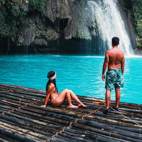 Two travellers on a bamboo raft at the base of Kawasan Falls with vivid turquoise water in Cebu Philippines - Contiki Cebu Bohol and Boracay Island Hopper Tour