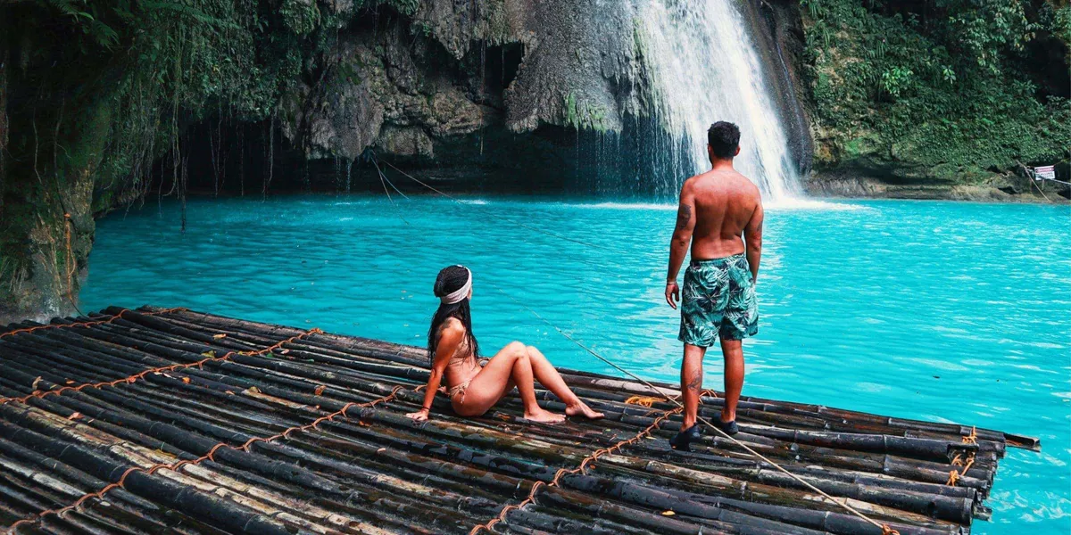 Two travellers on a bamboo raft at the base of Kawasan Falls with vivid turquoise water in Cebu Philippines - Philippines Island Hopping East Tour