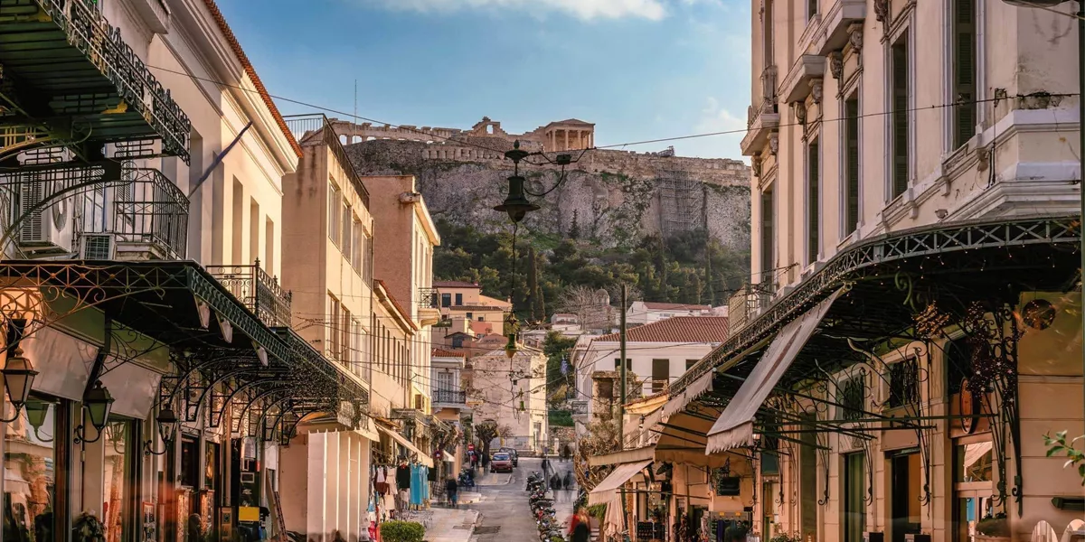 A lively street in Athens leads towards the Acropolis, with historic buildings, local shops and the ancient hilltop landmark in the distance - Greece: Ancient Wonders Tour