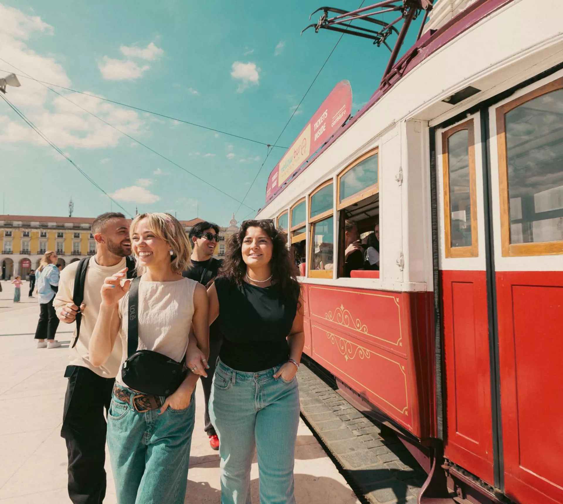 Young travellers next to a vintage red tram at Praça do Comércio Lisbon Portugal - Contiki Spain and Portugal Tour