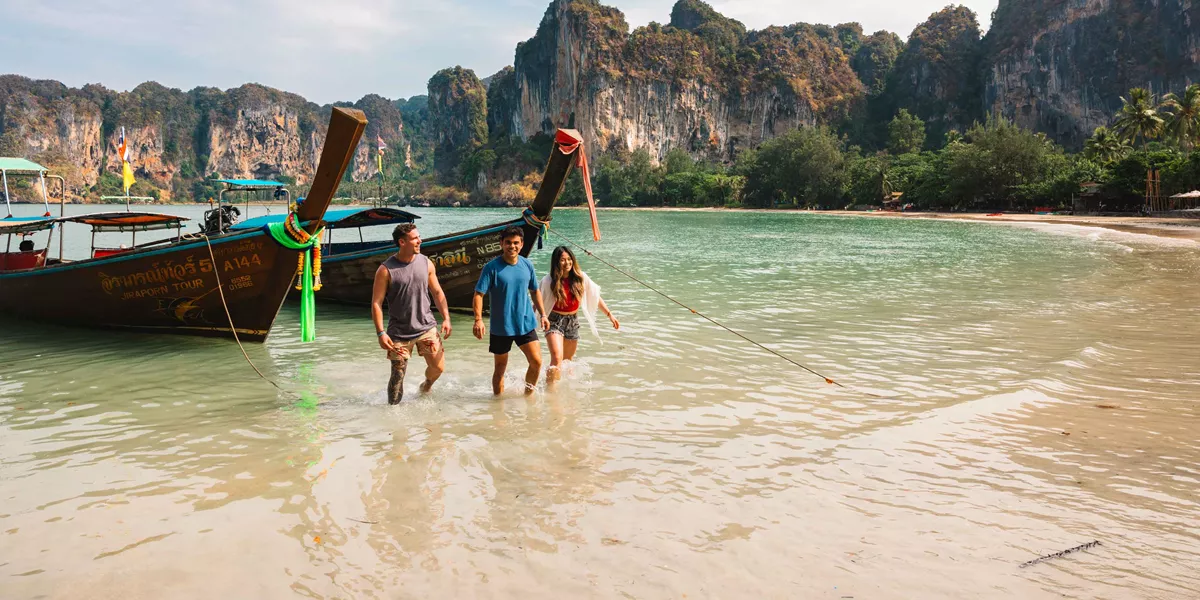 Group Of Young Travelers Getting Of Small Boat In Thailand