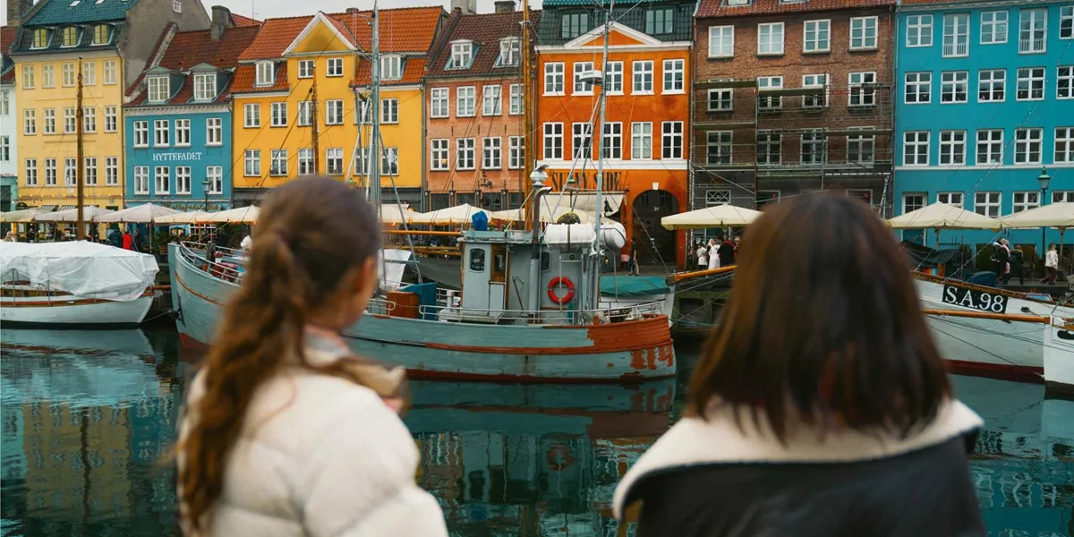 Travellers admire the colourful waterfront buildings and historic boats of Nyhavn in Copenhagen on the Contiki Best of Scandinavia Tour