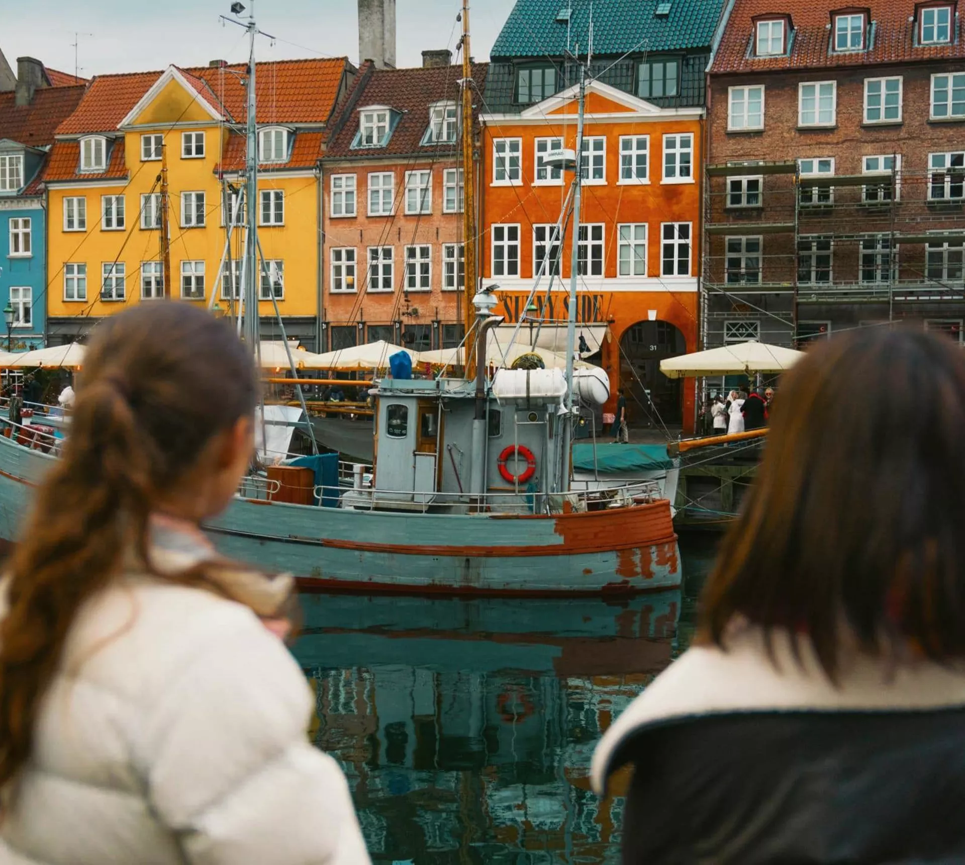 Travellers admire the colourful waterfront buildings and historic boats of Nyhavn in Copenhagen on the Contiki Best of Scandinavia Tour