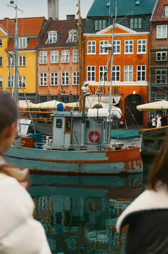 Travellers admire the colourful waterfront buildings and historic boats of Nyhavn in Copenhagen on the Contiki Best of Scandinavia Tour