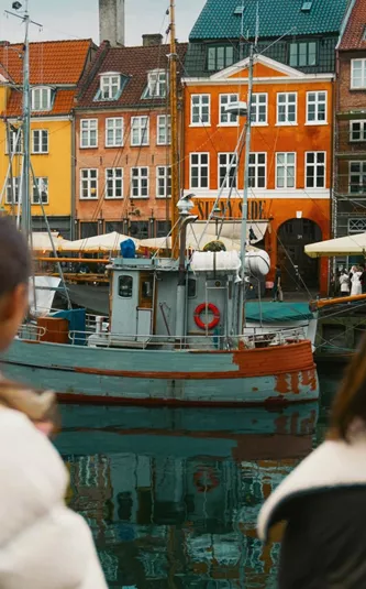 Travellers admire the colourful waterfront buildings and historic boats of Nyhavn in Copenhagen on the Contiki Best of Scandinavia Tour