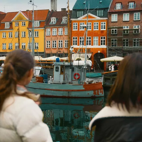 Travellers admire the colourful waterfront buildings and historic boats of Nyhavn in Copenhagen on the Contiki Best of Scandinavia Tour