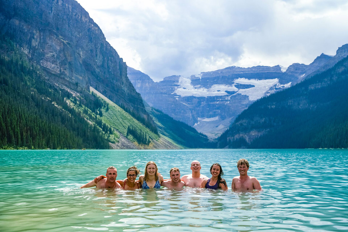 Group Of People In Blue Lake Surrounded By Mountains