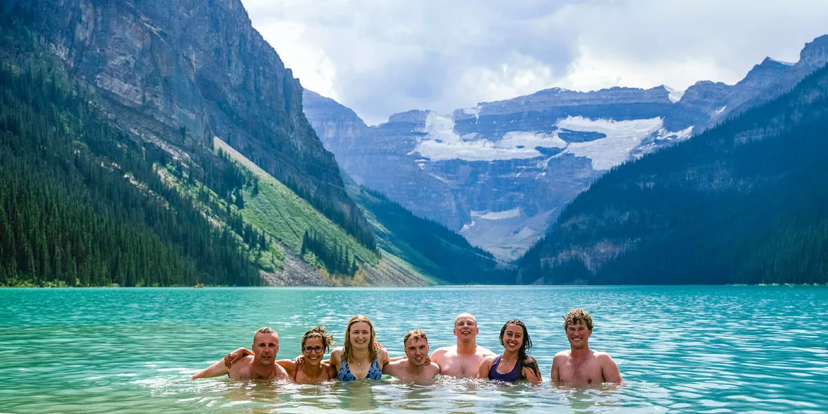 Group Of People In Blue Lake Surrounded By Mountains