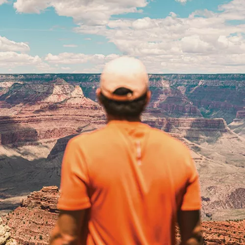 Traveller in an orange shirt overlooking the vast canyon landscape at Grand Canyon National Park, Arizona, USA.