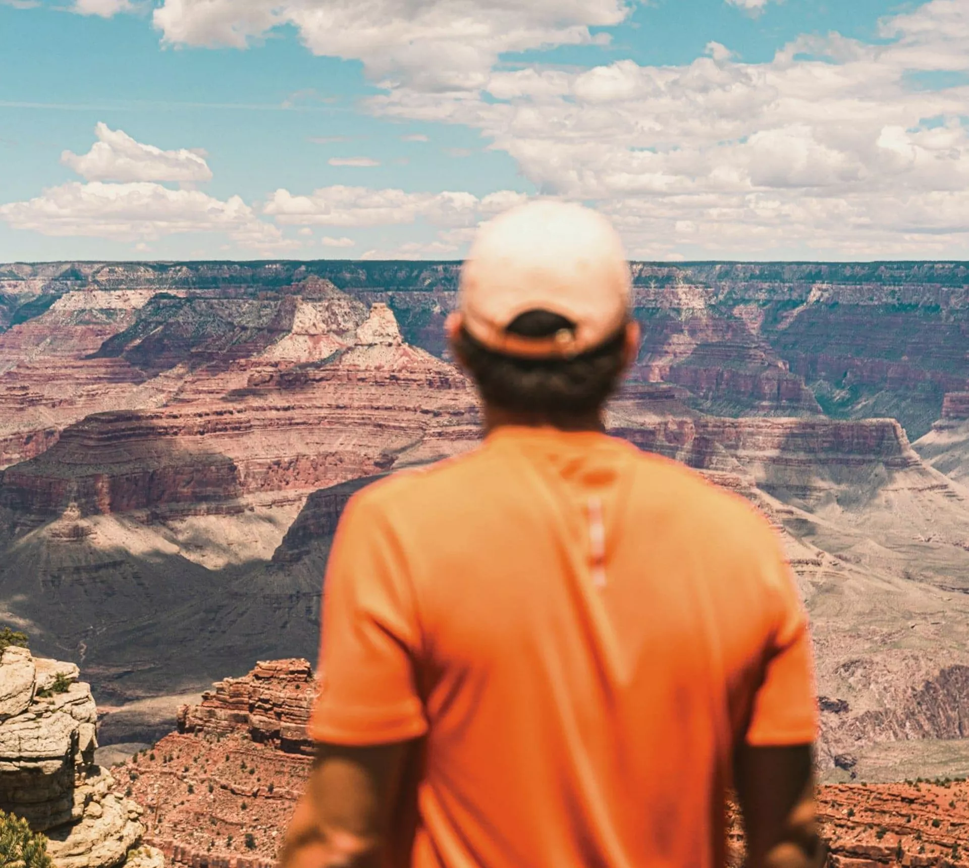Traveller in an orange shirt overlooking the vast canyon landscape at Grand Canyon National Park, Arizona, USA.