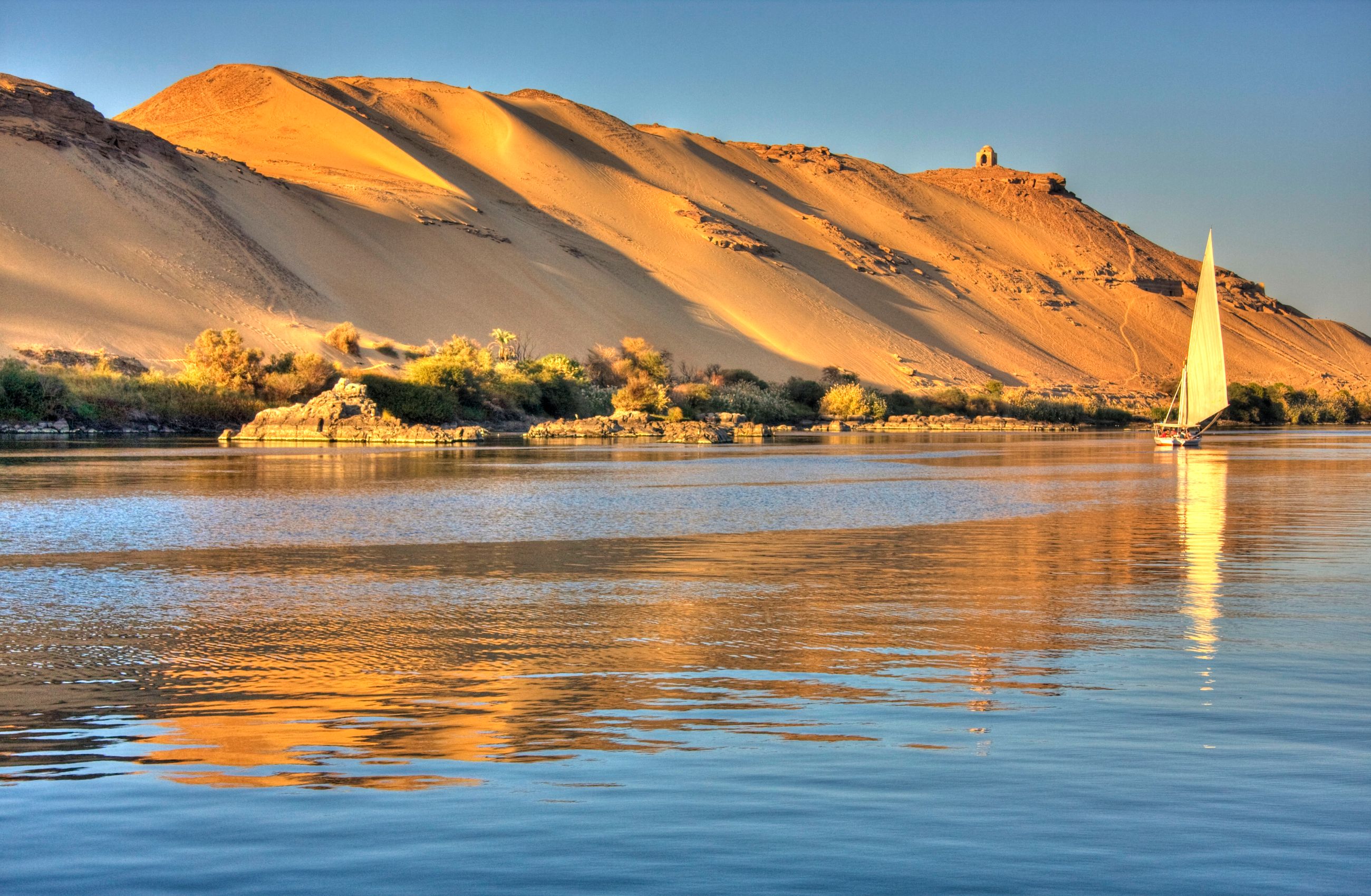 A sailing boat on the Nile River in Egypt. The river bank in a tall sand dune that slopes down to the water.