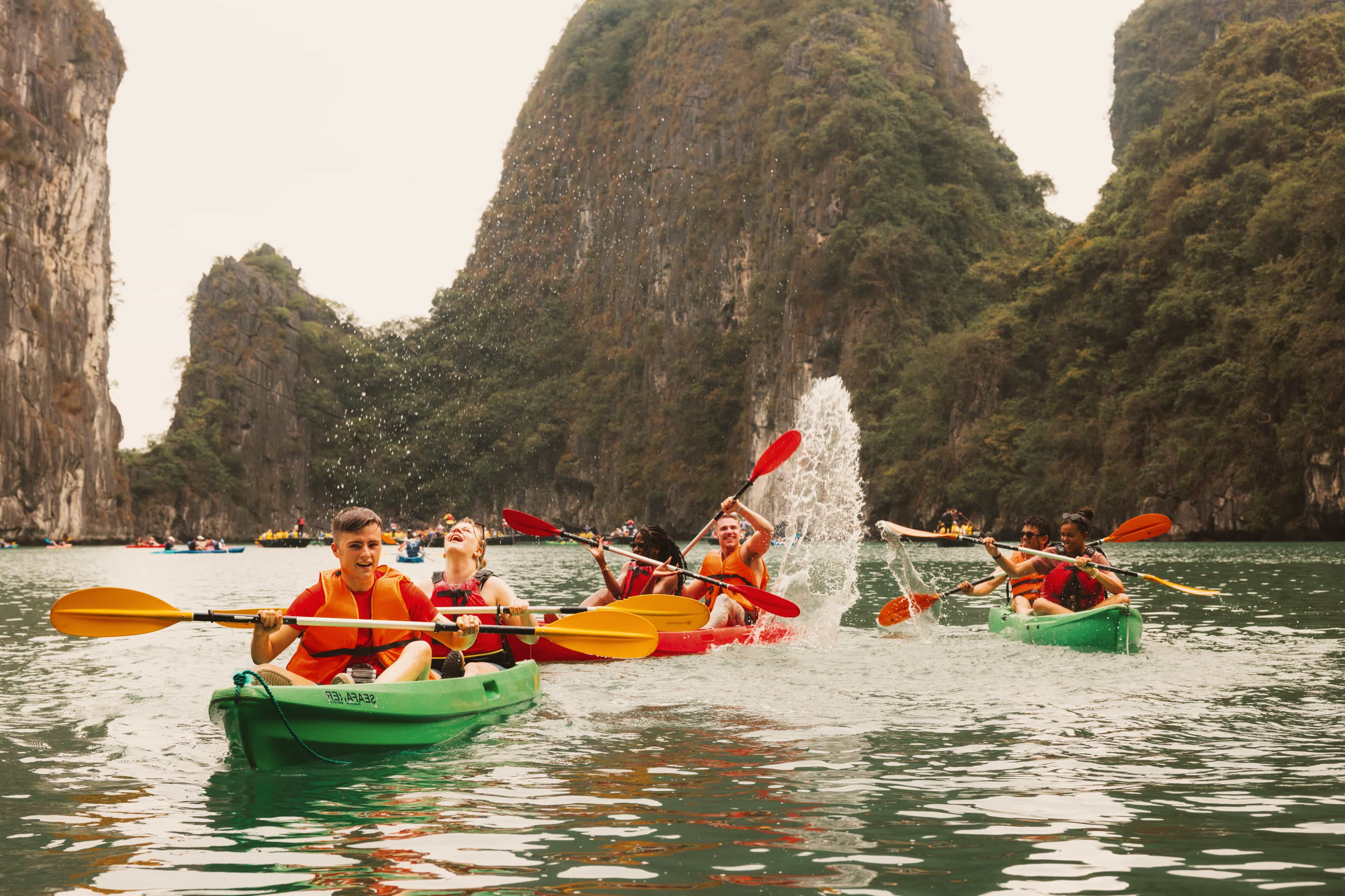 Travellers kayaking and splashing each other among the limestone karsts of Halong Bay, Vietnam.