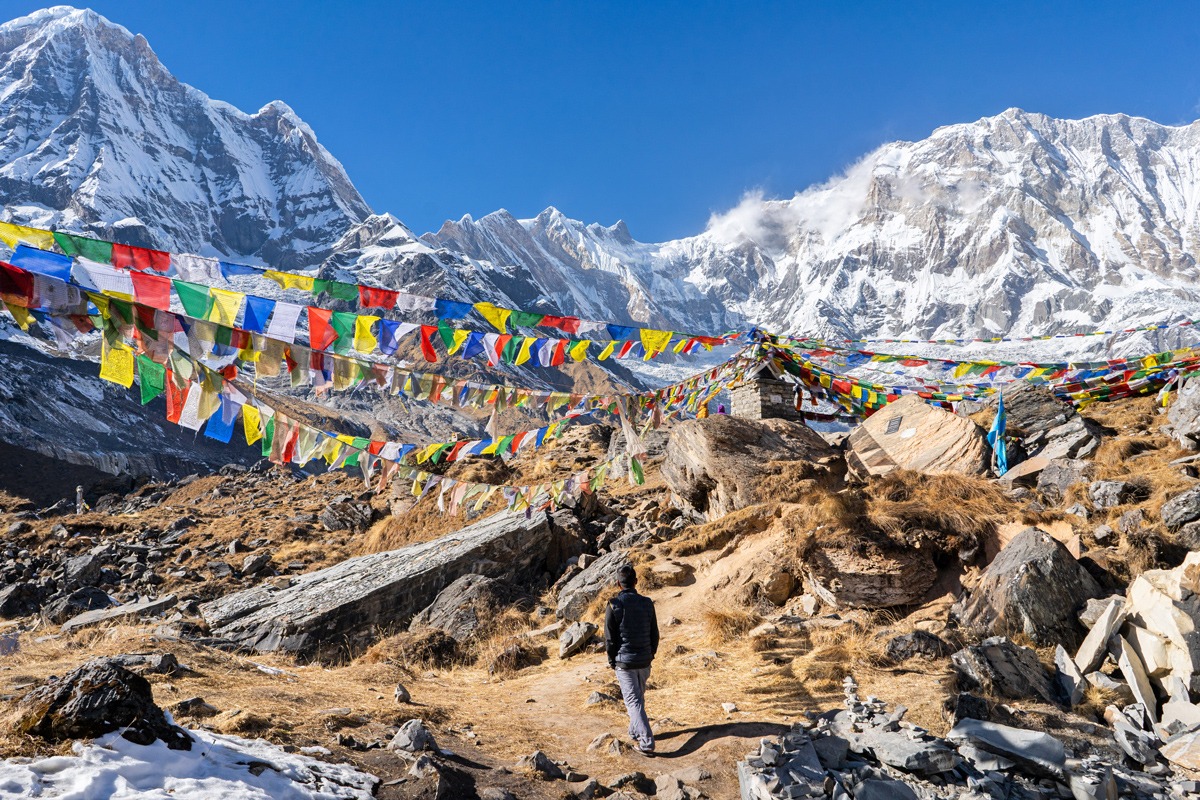 Man looking at snowy mountains colourful square fabrics hanging from a rope in Nepal.