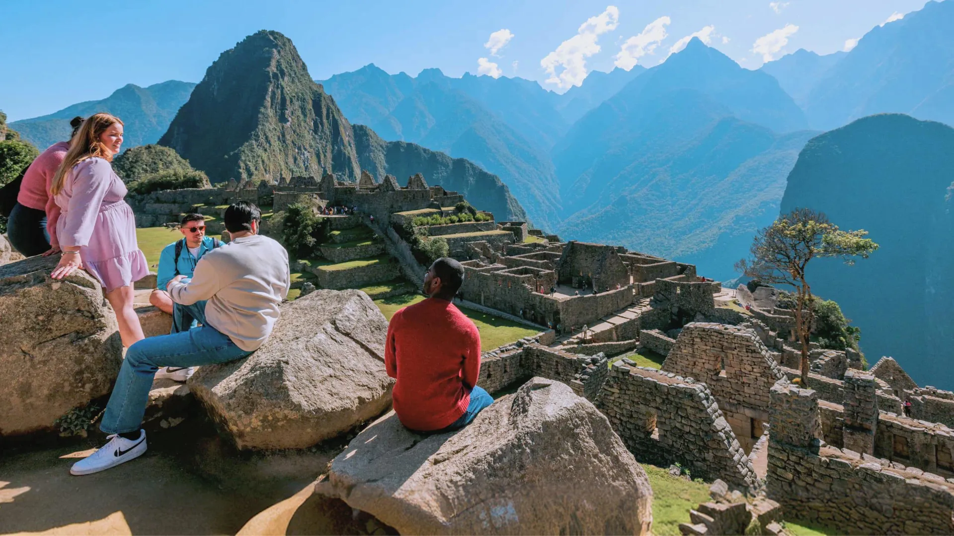 Group of young Contiki travellers sitting on rocks overlooking the ancient Inca ruins of Machu Picchu with Huayna Picchu mountain in the background Peru - Contiki South America Lima to Rio Tour