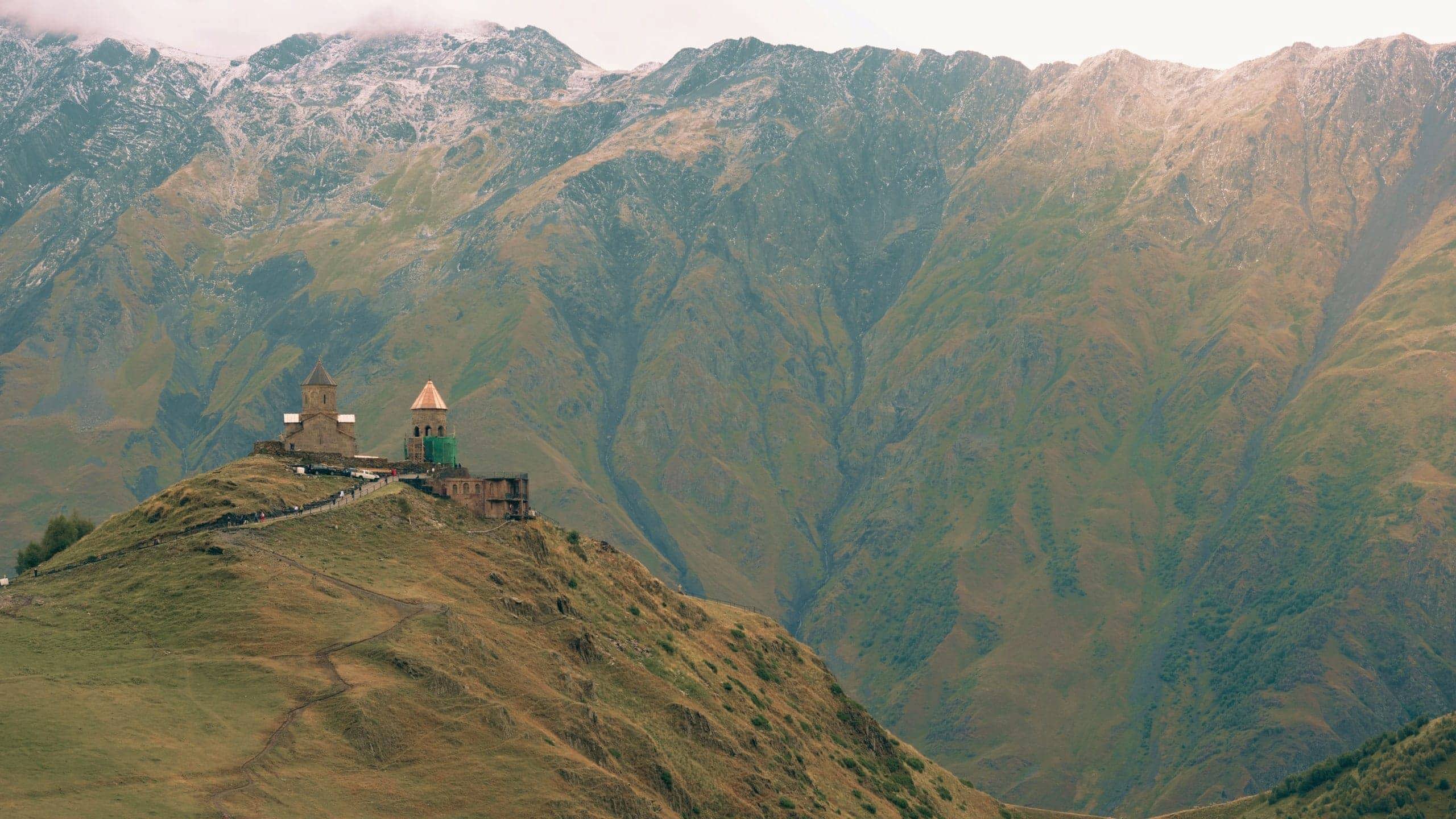 Gergeti Trinity Church sits atop a mountain ridge beneath the towering Caucasus Mountains on the Contiki Best of Georgia Tour