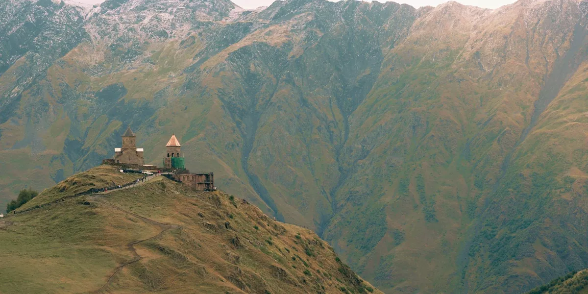 Gergeti Trinity Church sits atop a mountain ridge beneath the towering Caucasus Mountains on the Contiki Best of Georgia Tour