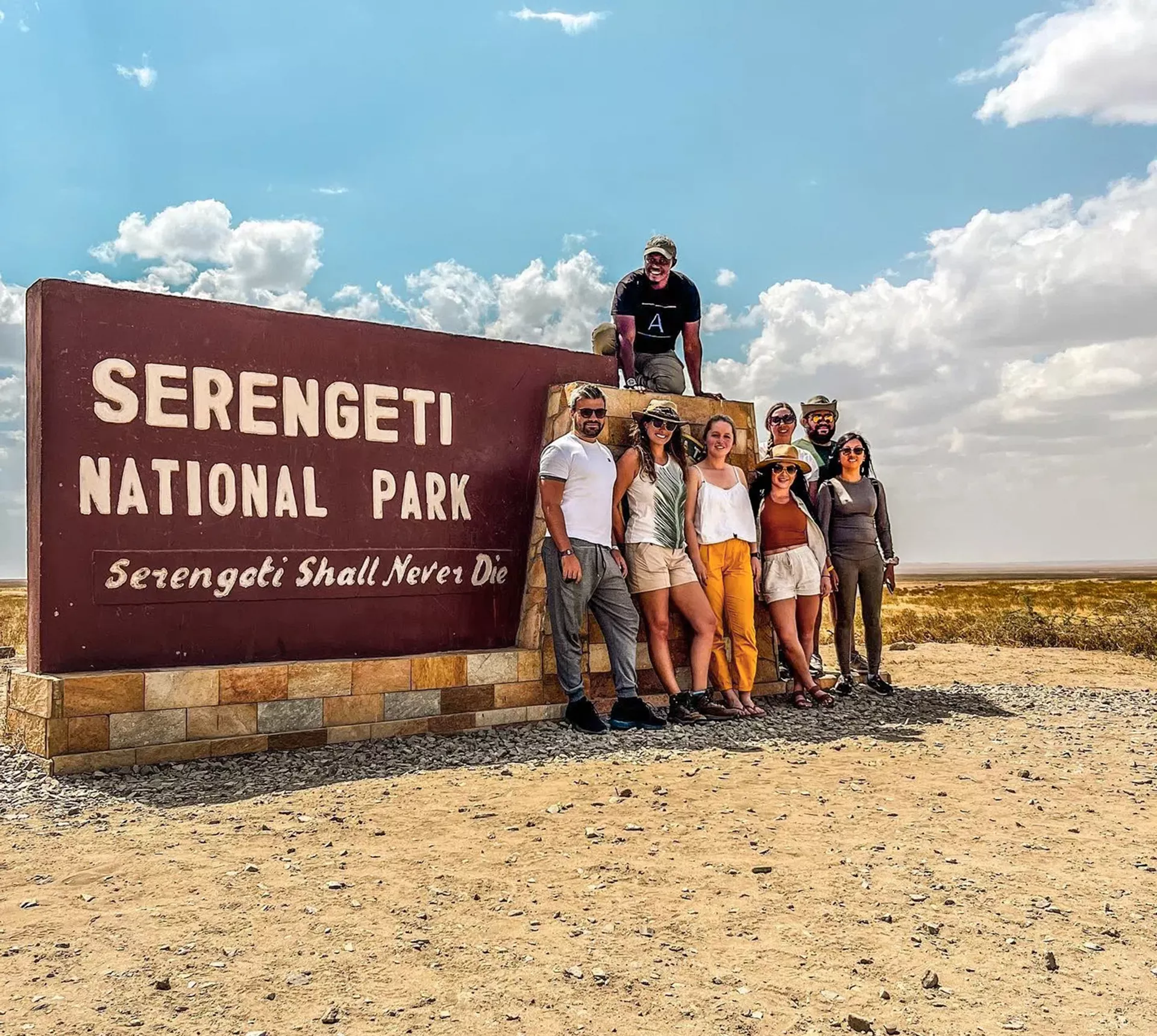 Group of travellers standing next to the entrance sign to the Serengeti National Park, Tanzania