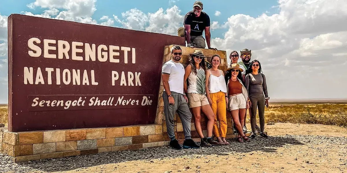 Group of travellers standing next to the entrance sign to the Serengeti National Park, Tanzania