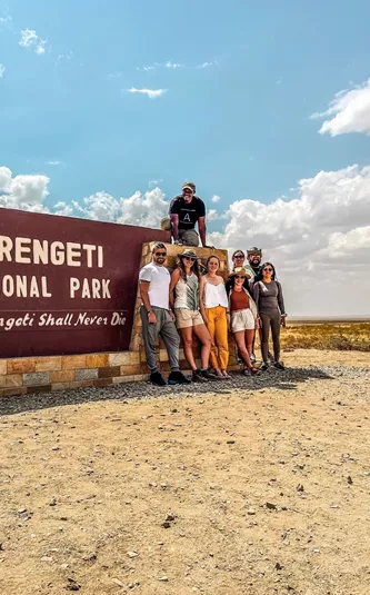 Group of travellers standing next to the entrance sign to the Serengeti National Park, Tanzania